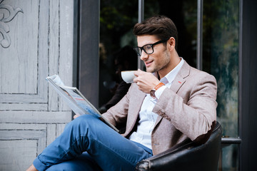 Smiling man drinking coffee and reading magazine in outdoor cafe