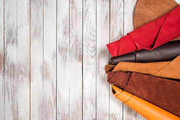 Brightly colored leather in rolls on white wooden background. Leather craft. Copy space. Top view.