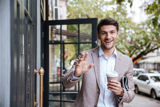 Businessman drinking cup of coffee and waving to someone