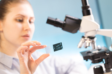 Woman in a laboratory microscope with microscope slide in hand. Research biopsy sample