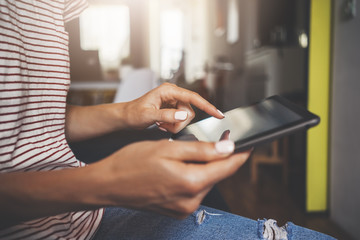 Close-up image of female hands using modern digital tablet, modern home interior in the backround, social networking concept, young hipster girl working from home via portable tablet, film effects