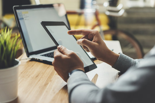 Close-up of male hands using modern digital tablet and laptop while working from home, young professional businessman working on devices at office, vintage orange bike in background