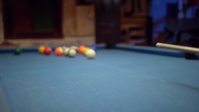 Pool break on a vintage worn out blue cloth pool table in slow motion. Sports game of billiards / 8 ball. Focus on the white cue ball.