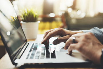 Close-up of male hands using modern laptop at home or cafe interior, young professional businessman working at his office via portable computer, sunshine, film effects