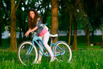 Joyful young woman on a bicycle in the green park at sunset