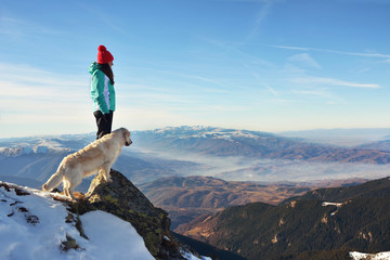 Girl with a golden retriever dog on top of a mountain during winter watching a beautiful landscape - Powered by Adobe
