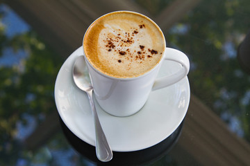 A cup of coffee in a white cup on glass background