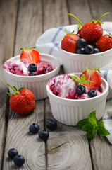 Ice cream with blueberries and strawberries in white bowl on rustic wooden background, selective focus, copy space