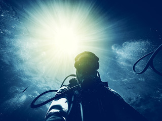 Man diving in the ocean with sun rays in the background.
