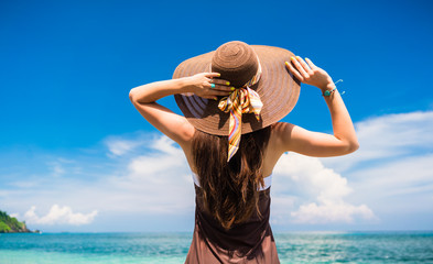 Frau im Sommer Urlaub mit Strohhut und Strandkleid genießt den Ausblick am tropischem Strand oder...