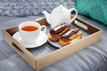 Cup of tea with pastry on tray on sofa