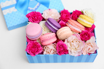 Tasty macaroons and roses in box on white background