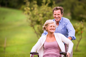 Senior man pushing woman in wheelchair, green autumn nature