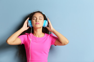 African American woman listening to music in headphones on grey background