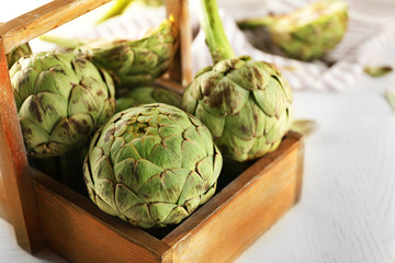 Obraz premium Artichokes in wooden container on light background