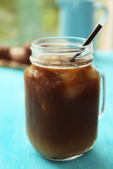 Glass jar of iced coffee on blue table