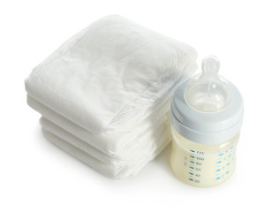 Baby bottle with milk and pile of diapers isolated on white