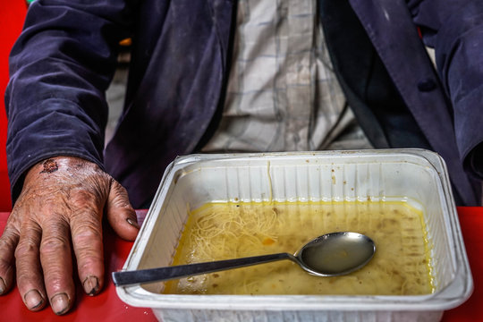 Old and wounded homeless man sitting at the table, with food. 