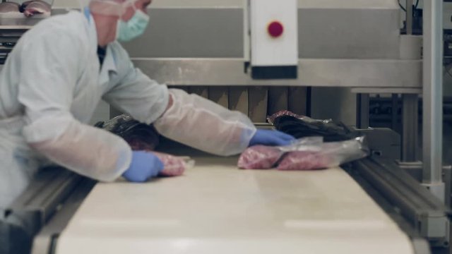 Industrial production of sausages. Production and packing of salami and bologna sausage in the meat industry. Hands of a worker in gloves packing forcemeat into plastic hermetic bag