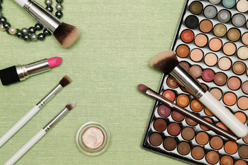 Make up set on light green background. Eyeshadow palette, brushes and lipstick.