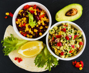 Ingredients for vegetarian tacos with guacamole, corn, black beans and red peppers. On black background, top view.