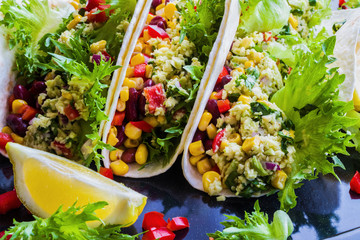 Vegetarian tacos with guacamole, corn, black beans and red peppers. On black background.