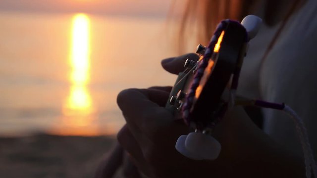 Woman Playing Guitar at Sunset by the Sea. Closeup.
