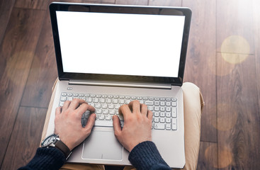 Photo of a man's hands using a laptop at home on his knees, young male student typing on computer