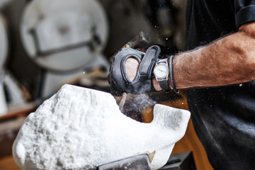 Close up of senior sculptor hands working on his marble sculpture in his workshop with hammer and...