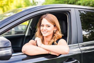 Fototapeta na wymiar Smiling young pretty woman in the black car. Concept of travel, rent car or buying car.