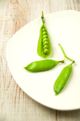 Green pea pods on the  big white plate.