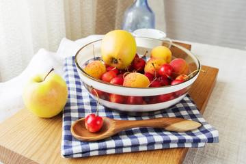 Composition of fruits and berries. Reason for the longevity is apples, cherries, apricots. Fruits and berries in a bowl on a checkered napkin on the table. Fruits and berries on a wooden cutting board