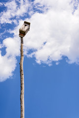 Old wooden birdhouse on a wooden post on the background of beautiful blue sky and clouds