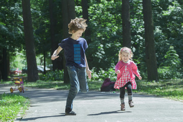 Laughing sibling children playing tag and running on park asphalt footpath