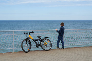 Obraz premium Мальчик с велосипедом смотрит на море стоя на набережной промеданте