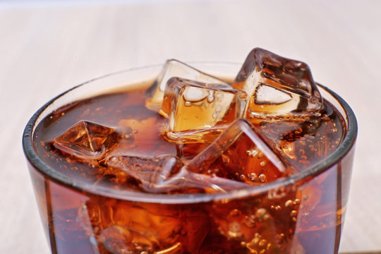 Glass of cola with ice on light wooden background