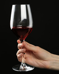 Female hand holding glass of red wine on black background