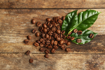 Coffee beans and green leaves on wooden background