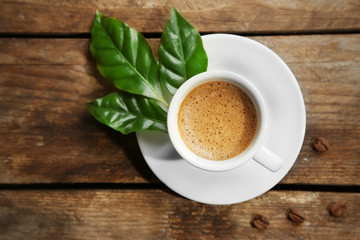 Cup of coffee with beans and leaves on wooden background