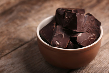 Chocolate bar pieces in a bowl on wooden background