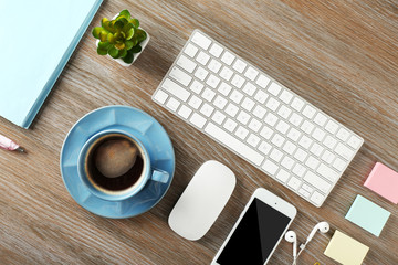 Keyboard, phone  and cup of coffee on a wooden desk background, top view