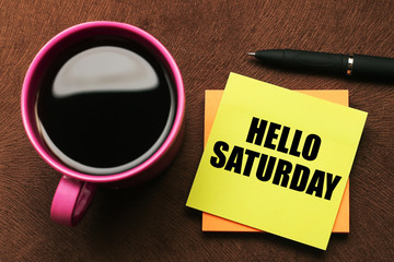 Hello Saturday - text on sticky note with a pen and cup of coffee