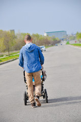 Obraz premium Handsome hipster modern walking with baby in pram outdoor in town. Vertical photo.