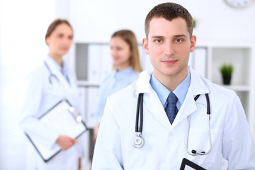 Fototapeta premium Friendly male doctor on the background with patient and his doctor in hospital. High level and quality medical service concept.