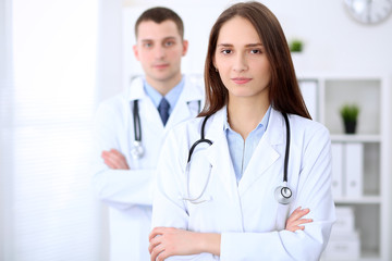 Young beautiful female doctor smiling  on the background with male doctor in hospital in hospital. High level and quality medical service concept.