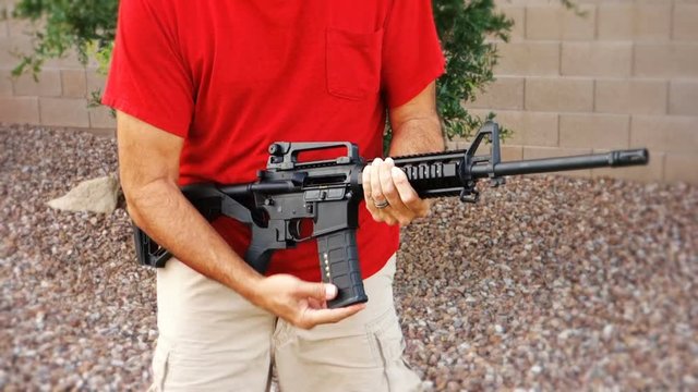 A man holding an AR-15 rifle shows how quickly the gun may be reloaded.	