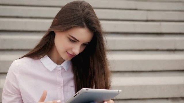 Young beautiful student girl using a tablet computer outside. Pretty teen woman reading on air.