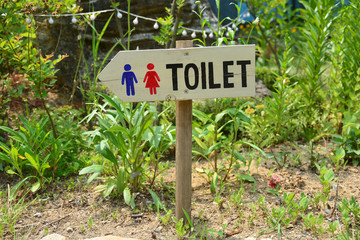 Wooden sign pointing way in garden to restrooms or toilets