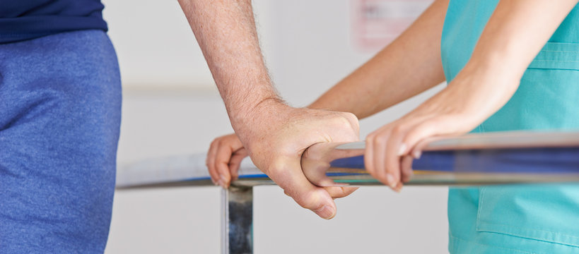 Hand eines Senioren am Geländer bei Physiotherapie
