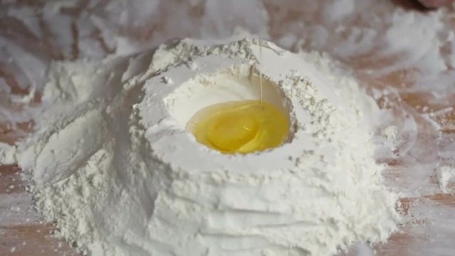 Close up of male hands adding egg to flour in slow motion